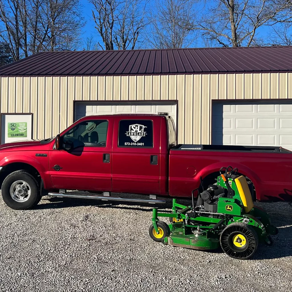 Red truck with S & L Lawncare logo on it. Next to green ride lawnmower